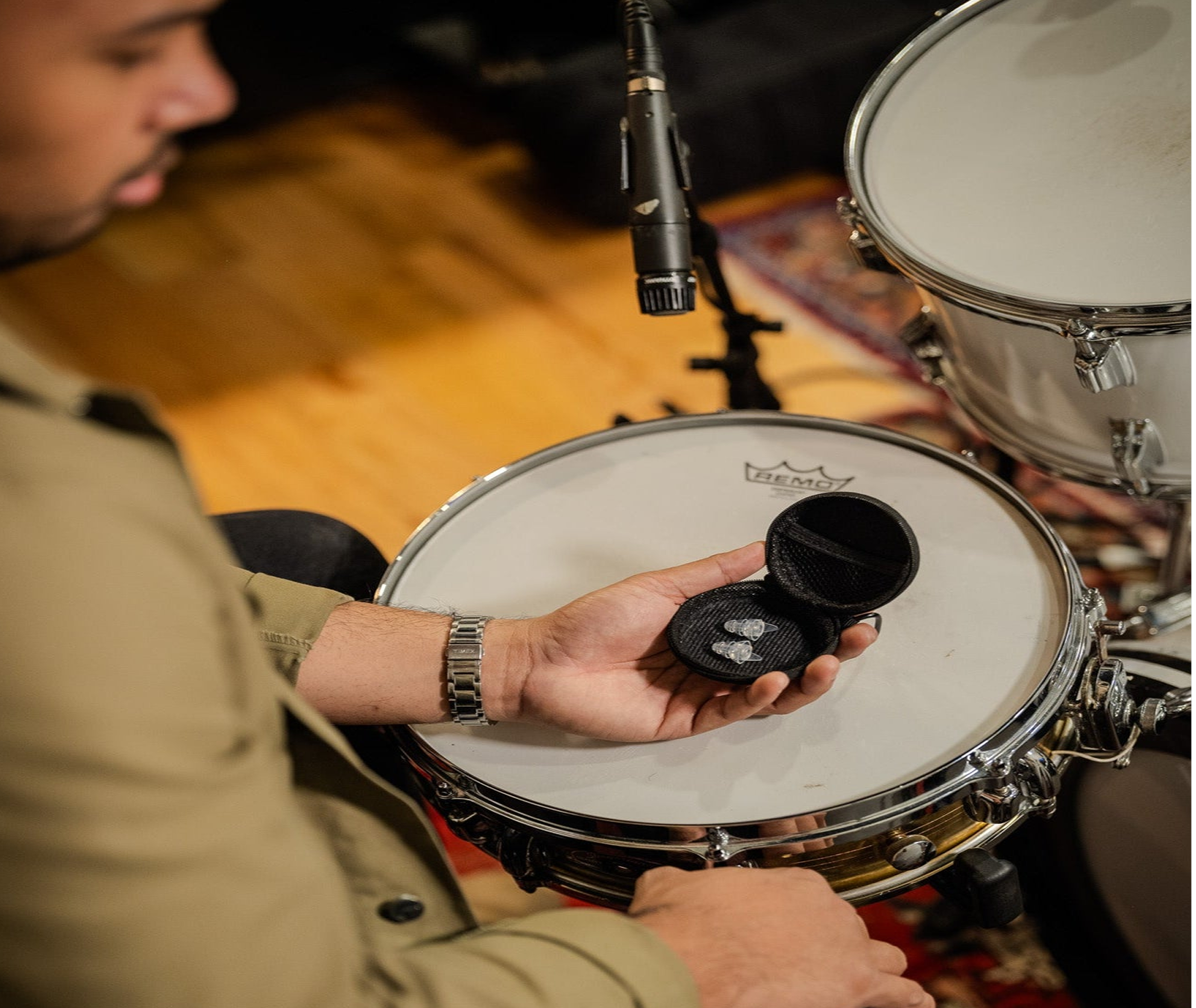 A person holds an open case of Ear-Goes high fidelity earplugs in front of a drum set on stage.