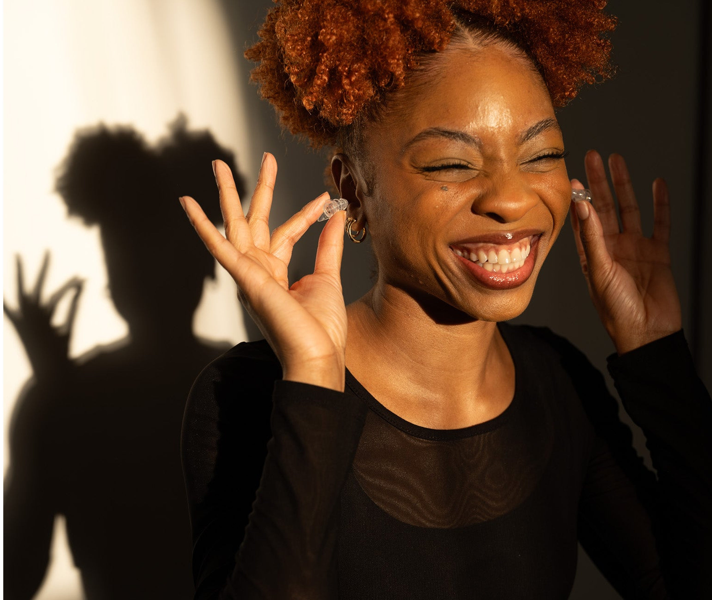 A smiling woman places Ear-Goes high fidelity earplugs in her ears.