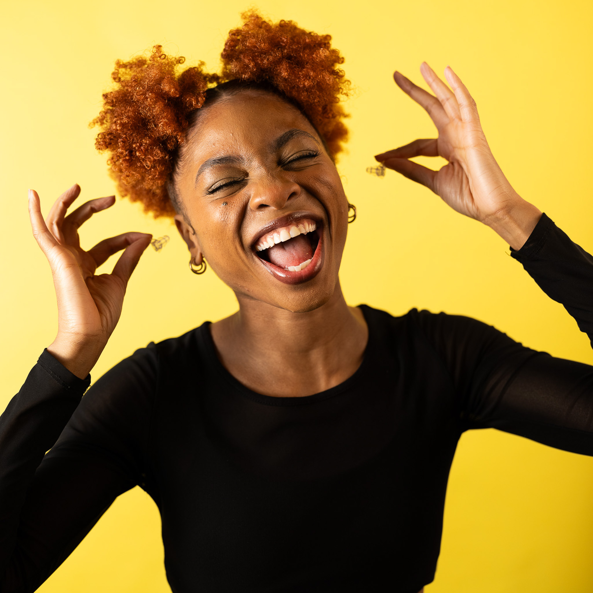 A smiling woman inserts Ear-Goes concert earplugs in both ears