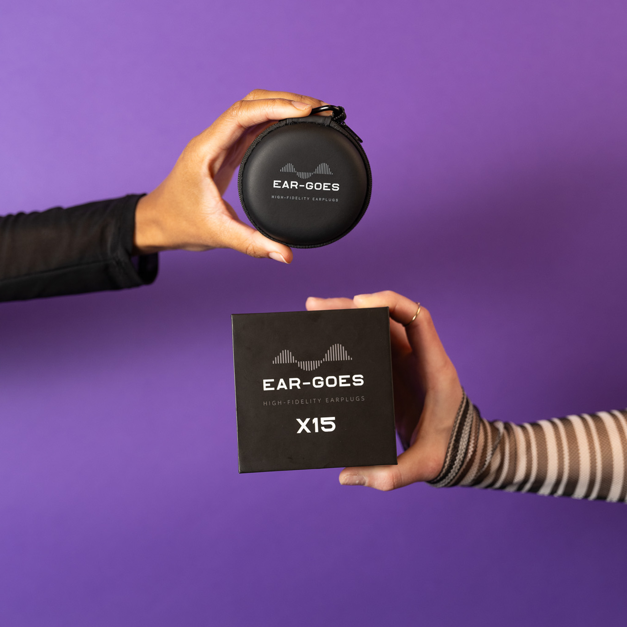 Two hands hold Ear-Goes earplug case and box in front of a purple background