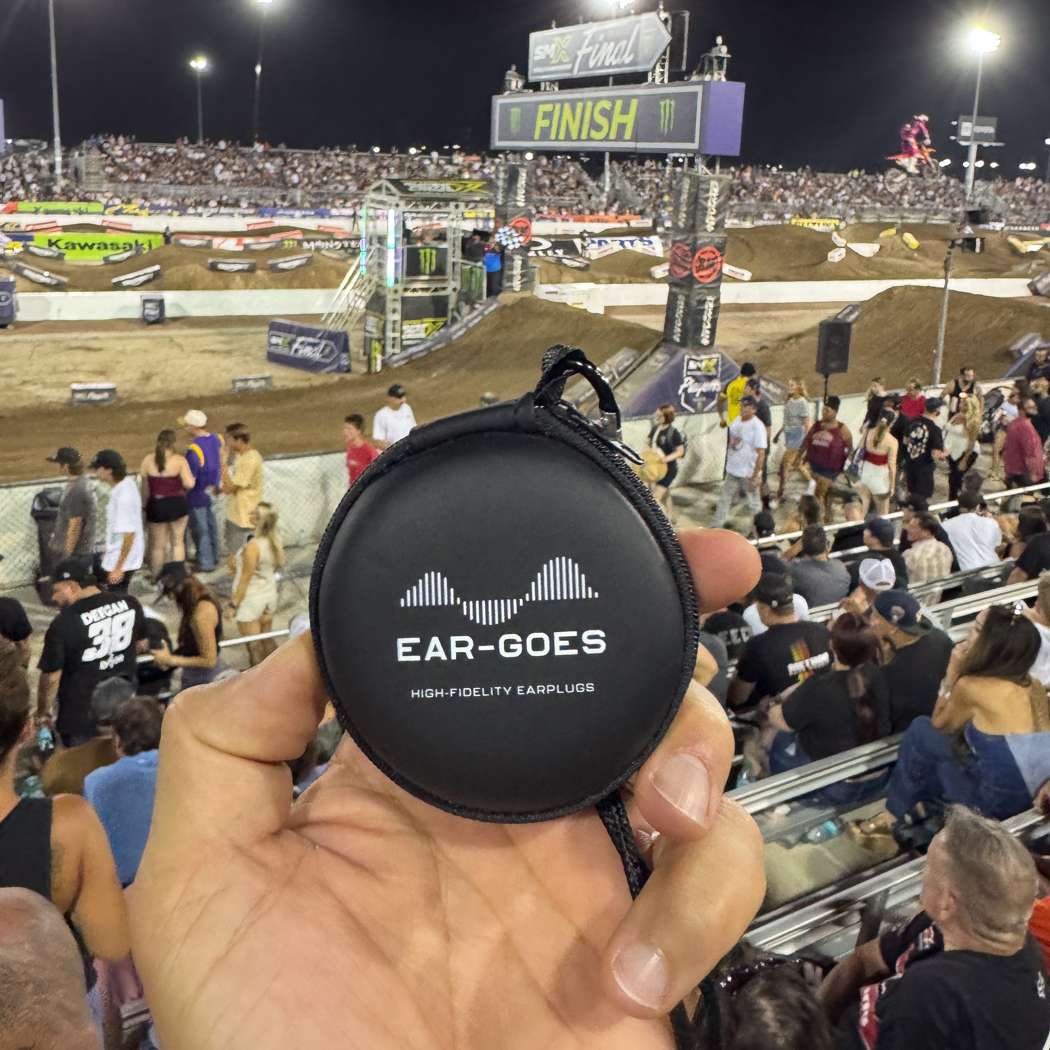 A hand holds an Ear-Goes earplug case at a motorcross race eent