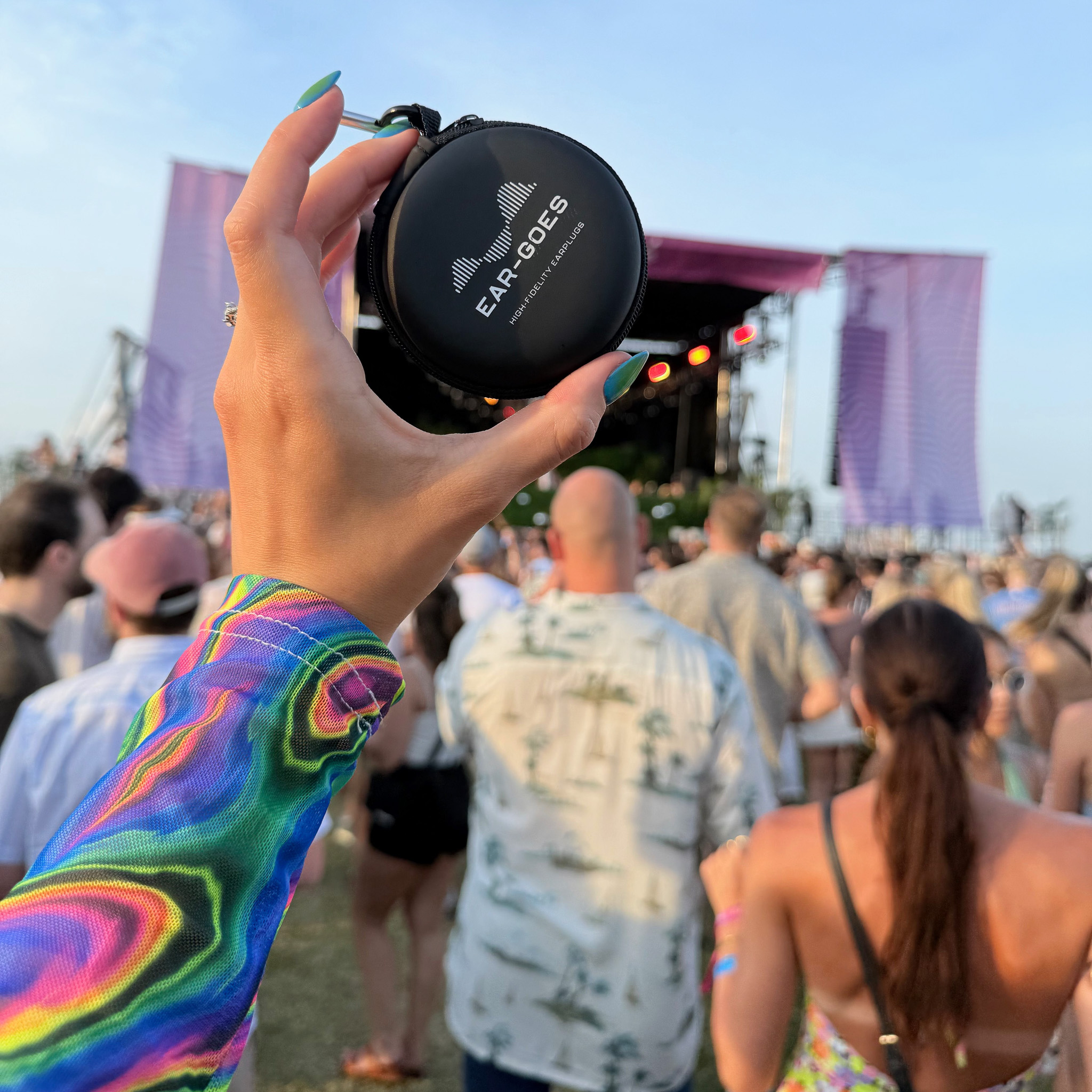 A hand holds a case of Ear-Goes earplugs at an outdoor music festival